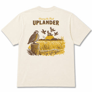 Back view of an off-white t-shirt featuring a brown and gold graphic of a Bobwhite Quail perched on a fence post and a covey of quail flushing in the distance, with text 'Chasing the Flush, Uplander'.