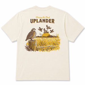 Back view of an off-white t-shirt featuring a brown and gold graphic of a Bobwhite Quail perched on a fence post and a covey of quail flushing in the distance, with text 'Chasing the Flush, Uplander'.