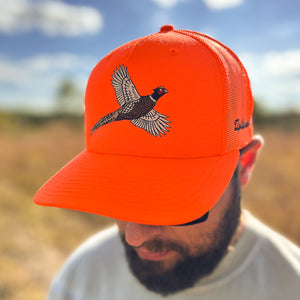 Man wearing a blaze orange snapback hat with orange mesh back featuring an embroidered flying rooster pheasant on the front, and 'Uplander' script on the side, worn outdoors.
