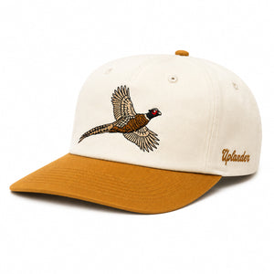 Cream-colored unstructured hat with a gold bill and an embroidered flying ring-necked pheasant on the front, and 'Uplander' script in gold on the side.