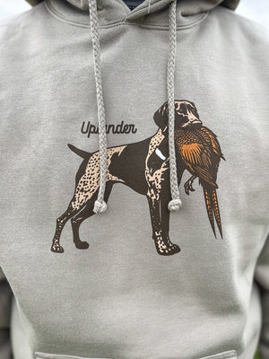 Close-up view of a man wearing a grey hoodie featuring a graphic of a liver and roan German Shorthaired Pointer holding a ring-necked pheasant in its mouth with Uplander branding.