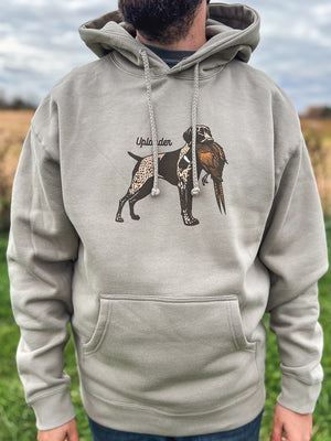 Man wearing a grey hoodie featuring a graphic of a liver and roan German Shorthaired Pointer holding a ring-necked pheasant in its mouth with Uplander branding, worn outdoors.