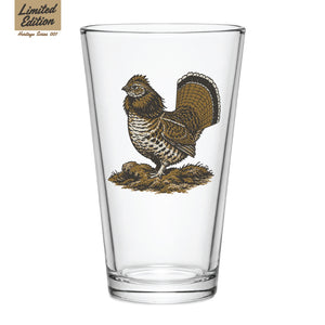 A clear pint glass featuring a detailed vintage-style illustration of a ruffed grouse with tail fanned, standing on a mossy mound, with a 'Limited Edition — Heritage Series 001' badge.