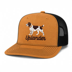 Caramel and black trucker hat with an embroidered liver and white English Springer Spaniel and 'Uplander' script in brown.