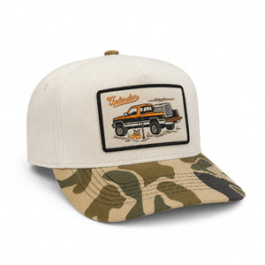 Cream-colored trucker hat with a camouflage bill and an embroidered patch featuring a vintage pickup truck and upland hunting gear.